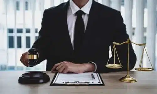 A personal injury lawyer raising a gavel over a soundblock at his desk while reviewing files for a client's case.
