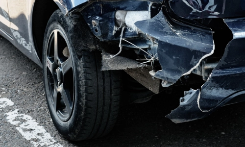 The torn bumper of a dark blue car damaged in a road accident.