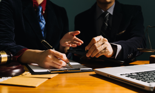 A shot of two personal injury lawyers discussing the details of a case in their Astoria, New York office. Both point to a clipboard with their pens