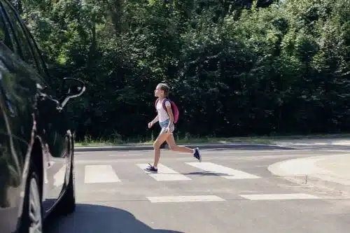 A young girl is crossing the street in front of a car.