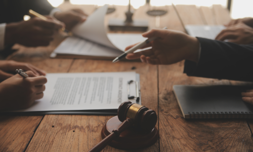 A closeup of a team of lawyers' hands on a desk as they discuss documents for a client.