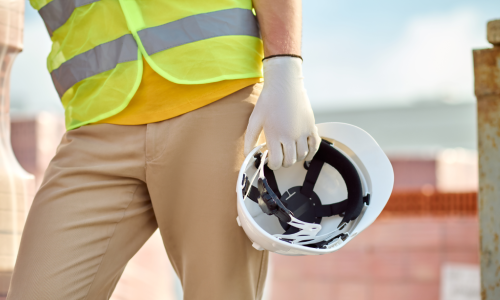 A hardhat worker carrying a white safety helmet in one hand and leaning for support.