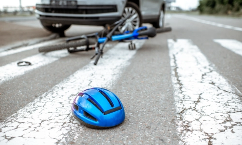 A bicycle and helmet lying on a marked crosswalk in front of a vehicle, illustrating the scene of a bicycle accident.