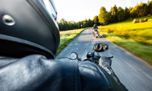 Motorcycle accident context showing a view of a motorcyclist riding on a country road, following another rider, capturing speed and potential risk factors.