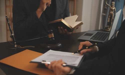 Personal injury lawyer consulting with a client at a desk, with legal documents, a gavel, law book, and Lady Justice statue, symbolizing legal representation.