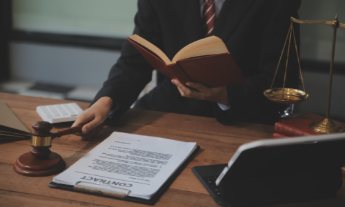 A lawyer reading a book and holding a gavel in his right hand next to a copy of a client's insurance contract.