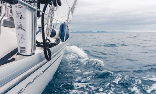 Close-up view of a sailboat cutting through ocean waves under cloudy skies, representing a potential boat accident scenario at sea.