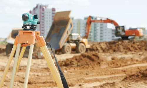 Construction accident scene showing a surveyor’s tripod with heavy machinery, including a dump truck and excavator, operating on a dirt site.