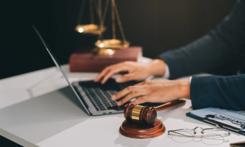  Defective product legal concept shown by a lawyer working on a laptop at a desk with a gavel, legal documents, and scales of justice in the background.