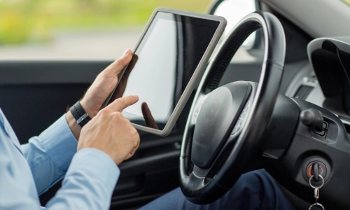 Distracted driving accident risk shown by a driver using a tablet inside a car, with hands off the wheel and eyes off the road.