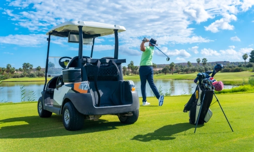 Golf cart parked on a green course beside a golfer mid-swing near a lake, illustrating a potential golf cart accident setting.