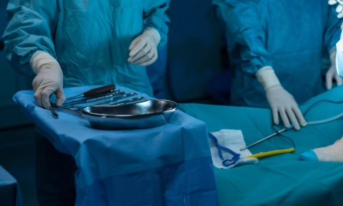  Surgeons in sterile gowns and gloves work in a brightly lit operating room with surgical instruments on a tray — involved in a Medical Malpractice case.