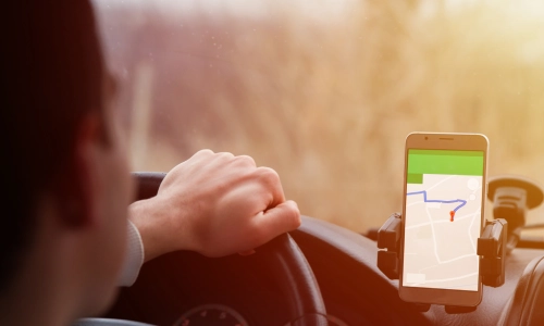 A person driving while following GPS directions on a smartphone mounted to the dashboard, involved in a rideshare accident, with one hand on the steering wheel.