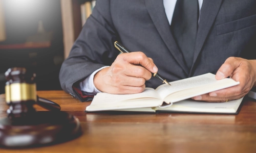  A close-up of a lawyer in a suit reviewing a legal book, sitting at a desk with a gavel in the foreground — suggesting involvement in a traumatic brain injury case.