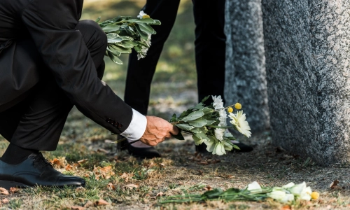 Wrongful death representation with mourners in formal black attire placing flowers at a gravesite, symbolizing grief and the pursuit of justice after a loss.