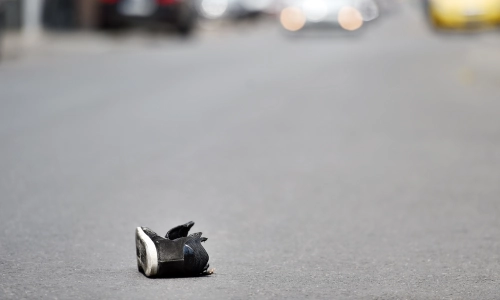 A single child’s shoe lying in the middle of a road with blurred cars in the background, suggesting a hit and run accident.