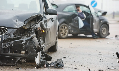 Two heavily damaged cars are shown after a serious collision on a city street, with one driver on the phone—highlighting the chaos and confusion that can follow an Uninsured Motorist Accident.