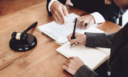 Two individuals at a wooden desk discussing and signing legal documents, with a gavel visible, symbolizing a personal injury legal consultation.