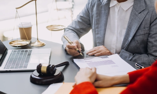 Personal injury attorney discussing legal documents with a client at a desk, with a gavel, justice scales, and a laptop visible in the background.