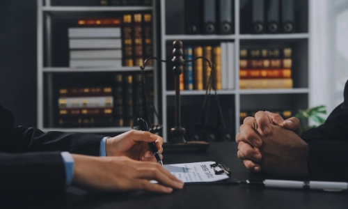 Personal injury legal consultation in a law office, showing a lawyer discussing a claim form with a client across the table, with legal books, scales of justice, and contract paperwork in view.