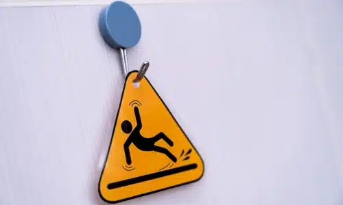 Yellow warning sign hanging on a wall indicating a slippery floor, applicable to a Savannah slip and fall lawyer.