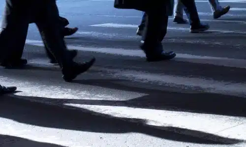 Multiple pedestrians walking across a crosswalk with long shadows on the road surface.