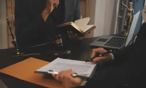 Two professionals in suits reviewing documents at a desk with a gavel, legal book, and Lady Justice statue, representing a consultation with a personal injury lawyer.