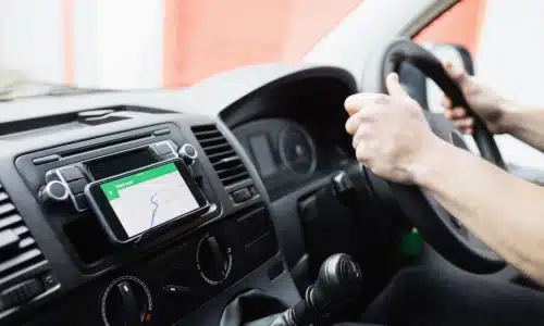 Driver holding the steering wheel of a vehicle with a GPS navigation app open on a mounted phone, representing a situation involving a rideshare accident.
