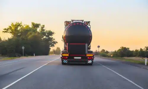 An early evening rear shot of a large tanker truck driving on a highway.