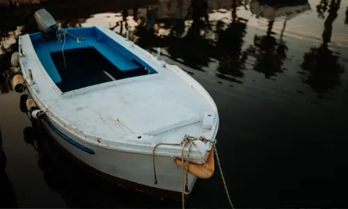 A white boat tied at the side of a small lake.
