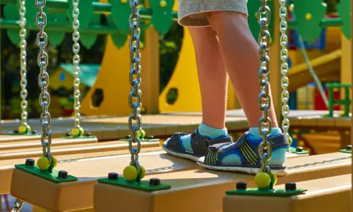 A toddler crossing a bridge built on playground equipment.