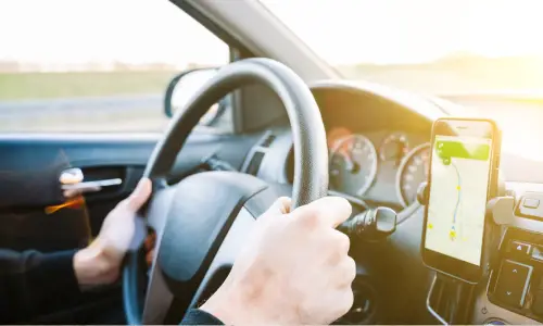 A closeup of a Lyft driver's hands on the steering wheel with the GPS in the foreground.