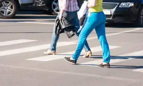 Two pedestrians crossing the street ahead of several cars stopped in the background.
