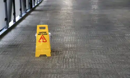 A yellow wet floor sign on stone flooring inside of a building.
