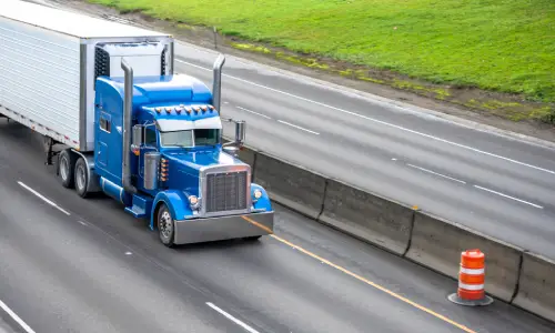 A large blue big rig driving at speed next to concrete barriers on a highway.