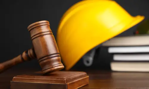 A yellow hardhat on a table next to a judge's gavel and resting on law books.