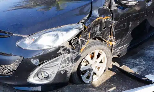 Damaged black car with a crumpled front fender and flat tire, showing visible scratches and impact marks from a collision, symbolizing the aftermath of a car accident