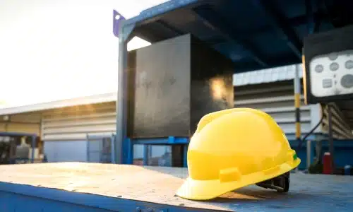 A yellow construction hard hat resting on a metal surface at a job site, representing safety concerns and legal implications in construction accident cases.