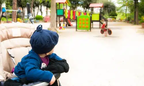A baby in a stroller looking toward a colorful playground, symbolizing concerns about safety and potential accidents in daycare environments.