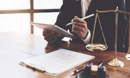 A lawyer reviewing documents on a tablet beside legal paperwork, a gavel, and the scales of justice, representing legal action in defective product cases.