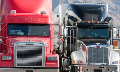 Two large commercial semi-trucks one red and one black parked side by side, highlighting the scale and presence of vehicles often involved in highway accidents.