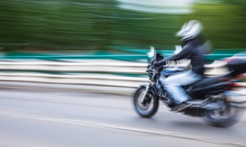 Motion-blurred image of a motorcyclist in a helmet riding at high speed on a road, representing the risk of motorcycle accidents.