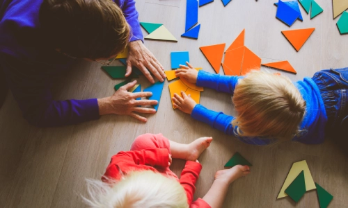 Adult and children playing with colorful puzzle pieces on the floor, applicable to a Columbus daycare injury lawyer.