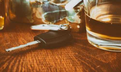 Car key next to a glass of whiskey on a wooden table, representing cases for a Columbus drunk driving accident lawyer.