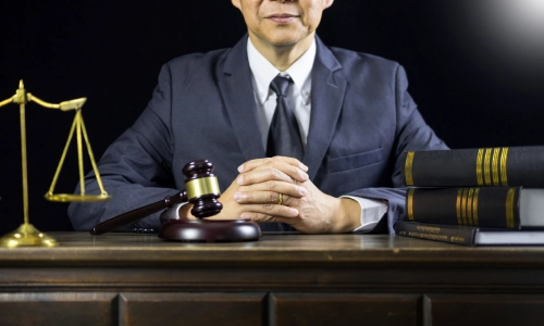 An Asian Gainesville Distracted Driving Accident Lawyer who is sitting down at his law office with both hand clasped on top of the table in front of him.