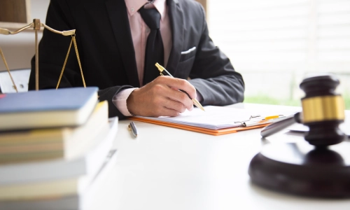A car accident lawyer writing on documents on a table with some books piled on top inside a Houston law office.