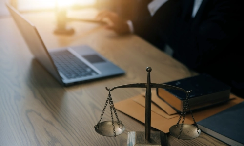 A negligence lawyer sitting in front of a laptop on top of a table inside a Houston law office with scales of justice in the foreground
