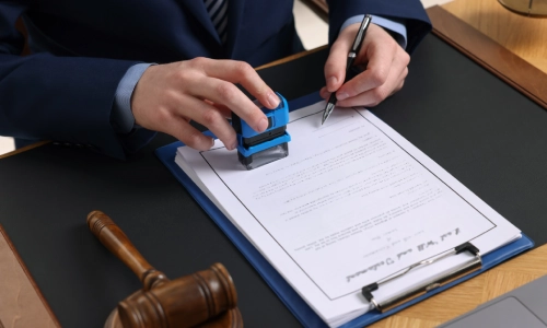 A rideshare accident lawyer holding a notary stamp in the right hand and a pen on the left above some files while sitting in a Houston law office