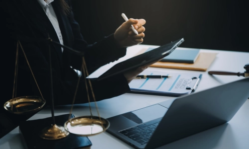 A professional in formal attire sits at a desk with legal tools, including a scale of justice, gavel, laptop, and documents symbolizing legal consultation or case preparation, possibly for a truck accident case.
