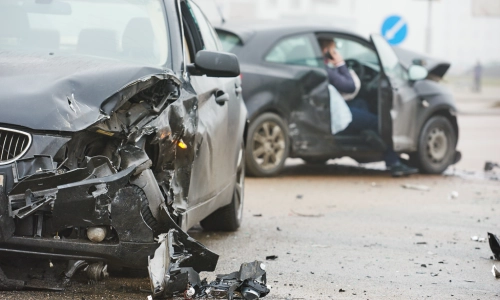 Two heavily damaged cars after a collision on a city street, with debris scattered across the road and a driver making a phone call illustrating the aftermath of an uninsured motorist accident.